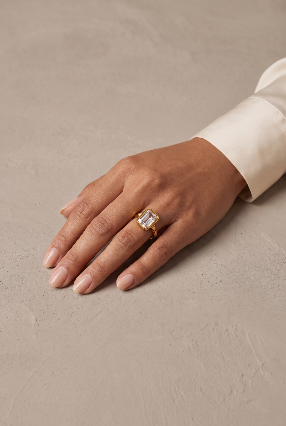 Emerald-cut crystal bezel ring in gold worn on the hand